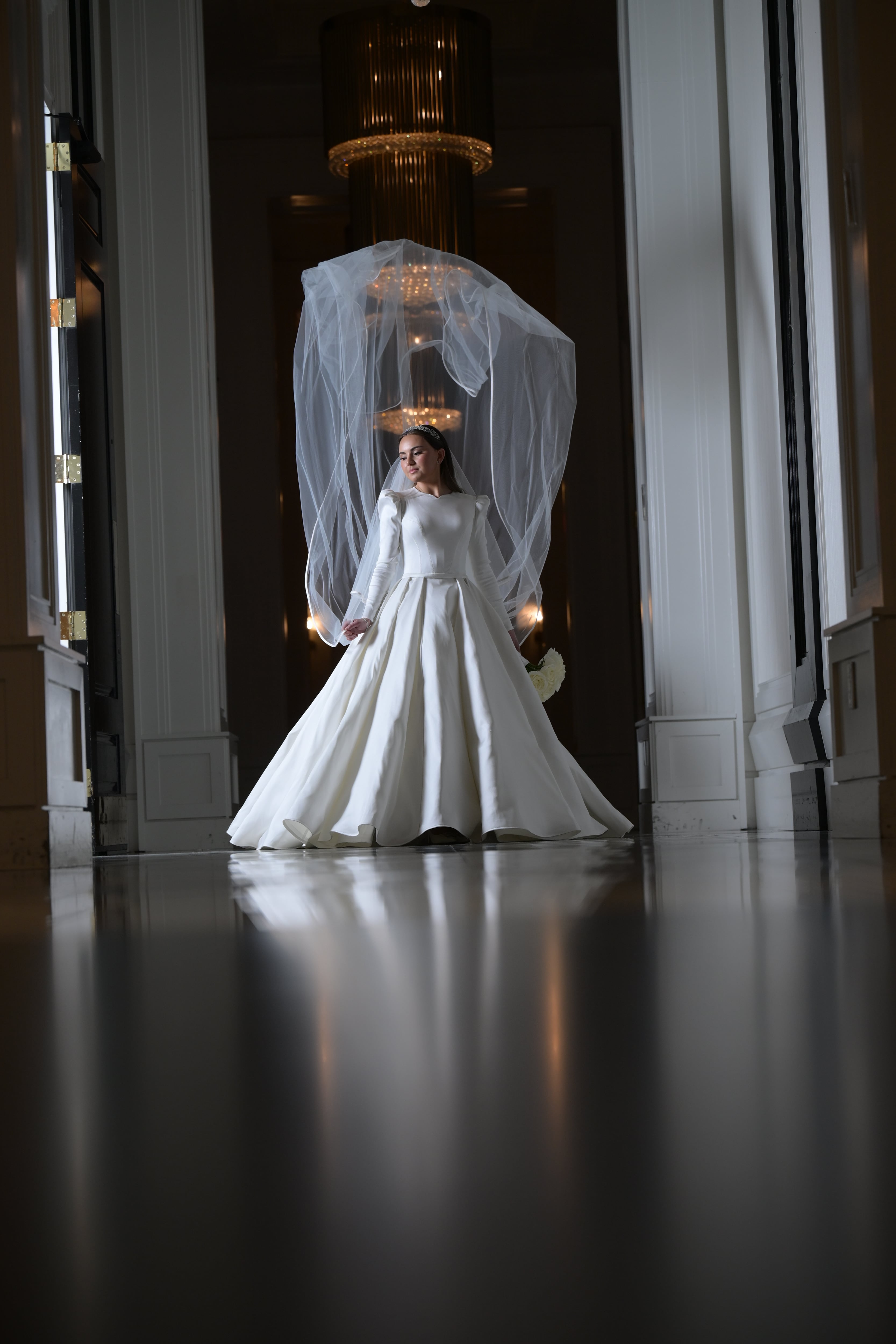 Bride centered in hallway under crystal chandelier