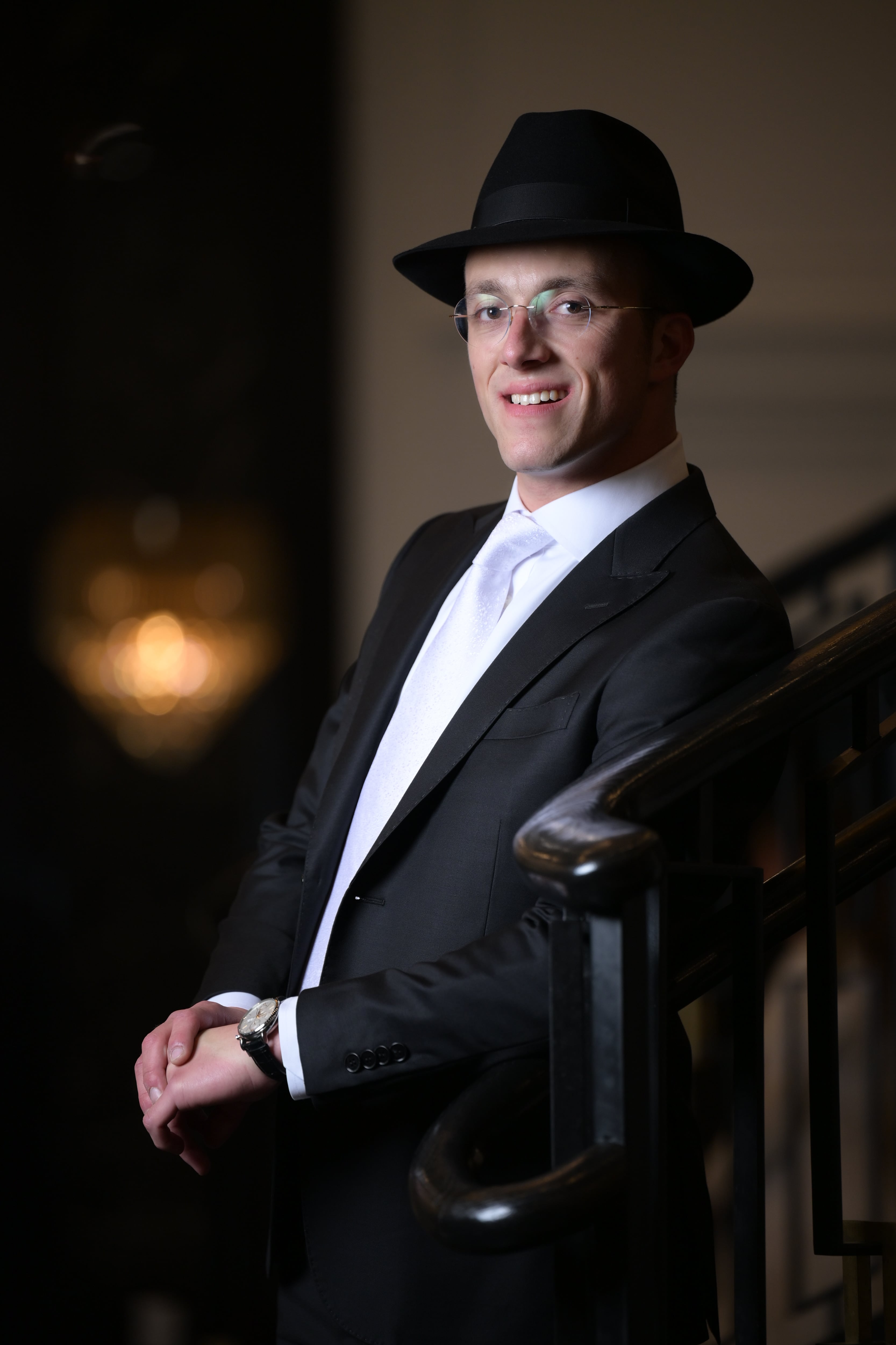 Groom portrait in fedora and glasses by railing