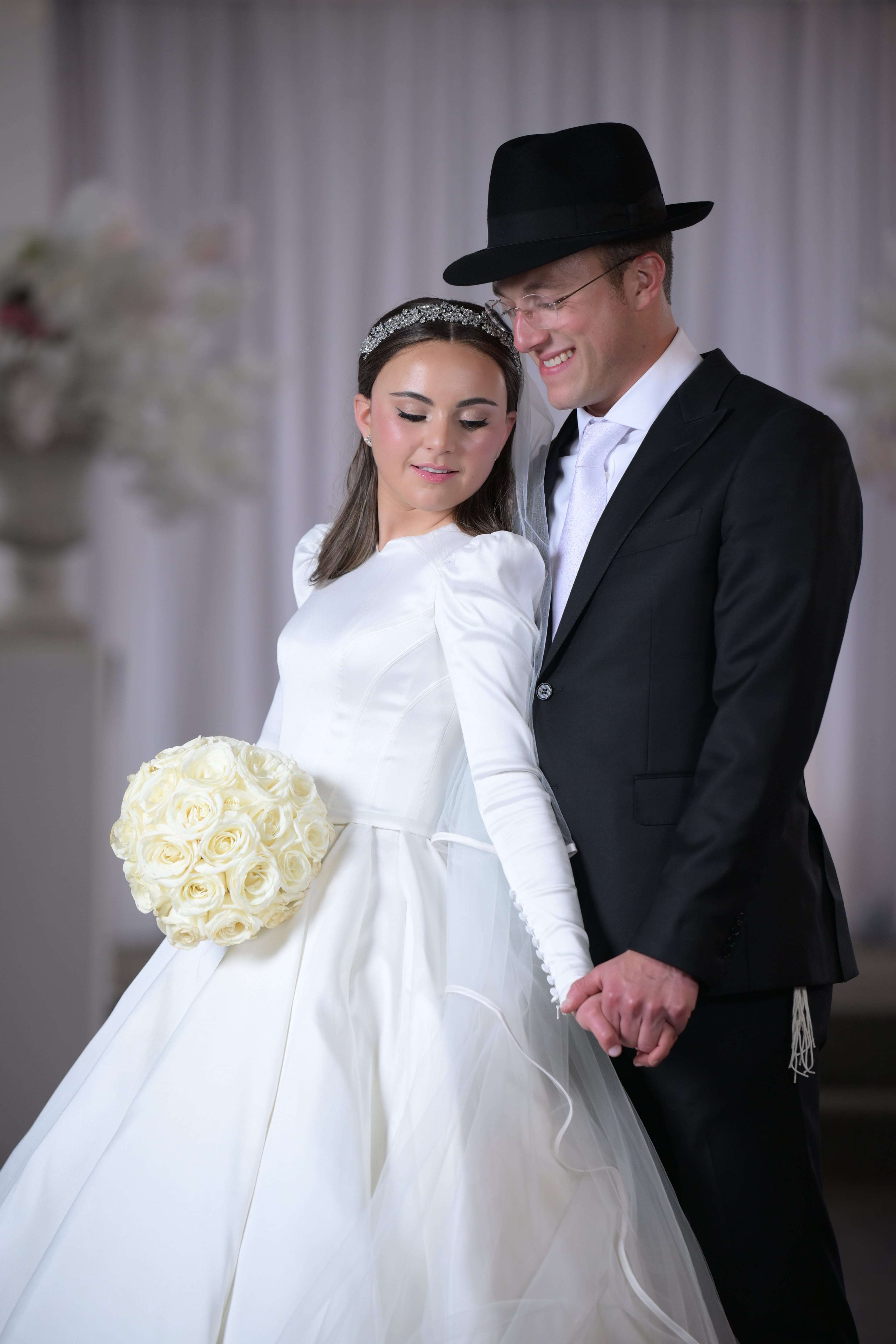 Couple hand-in-hand under white chuppah pillar